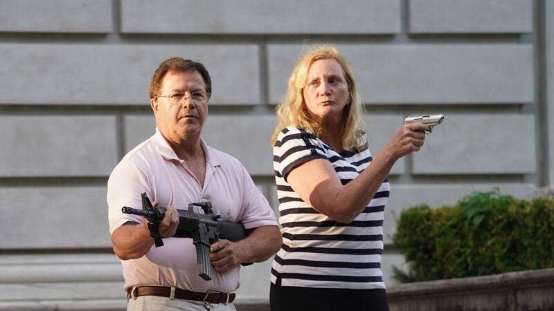 A husband and wife hold a pistol and a rifle as protesters walk past their house enroute to...